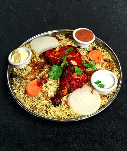 A tandoori chicken leg over saffron biryani rice on a steel thali