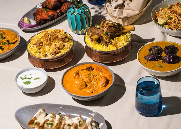 A long table laid with biryanis, curries, tandoori chicken and naan in bright daylight